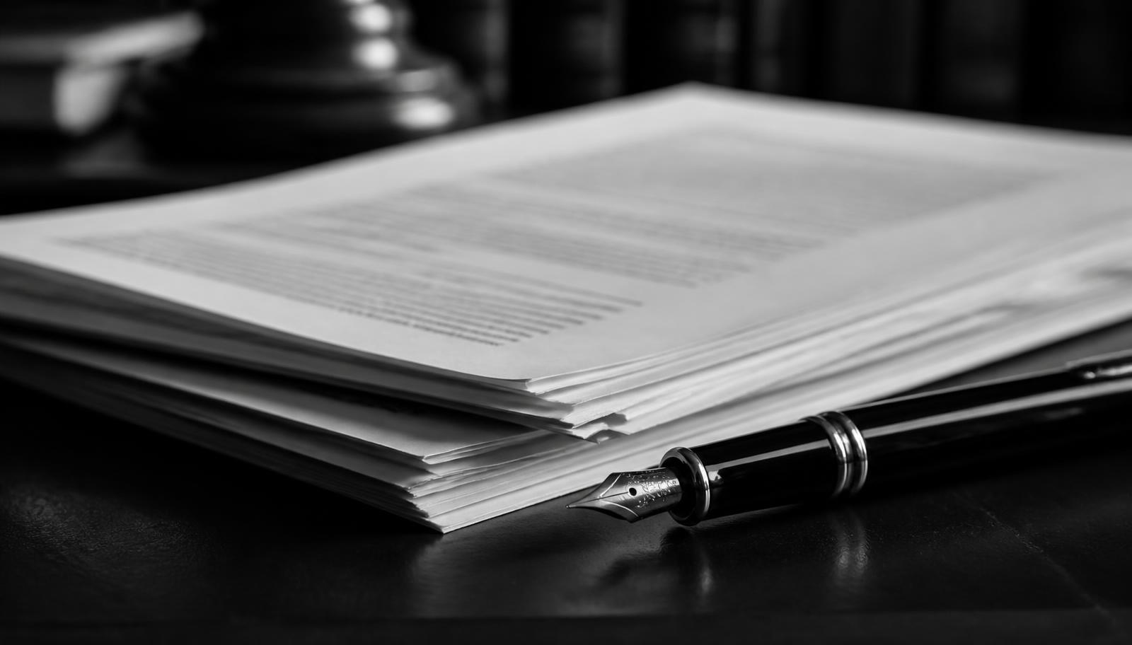 Stack of printed legal documents beside a fountain pen on a dark desk